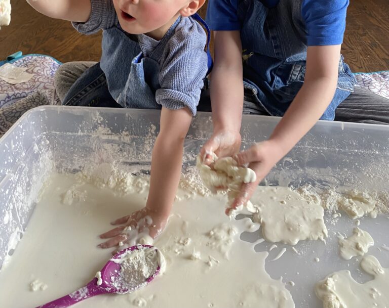 Children playing in sensory bin with flour and water.  The caregiver is encouraging exploration.  Hands-on learning is a vital means for children to explore, discover, and construct knowledge about the world around them.